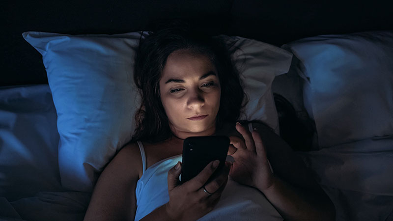 woman scrolling through social media in bed at night